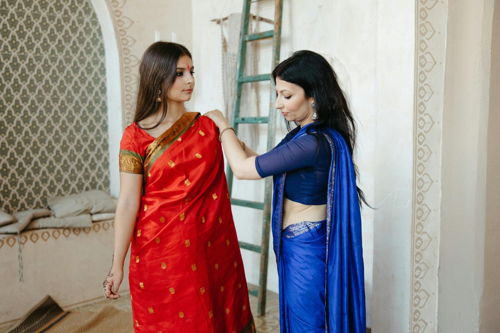Two South Asian women wearing traditional sarees and preparing indoors.